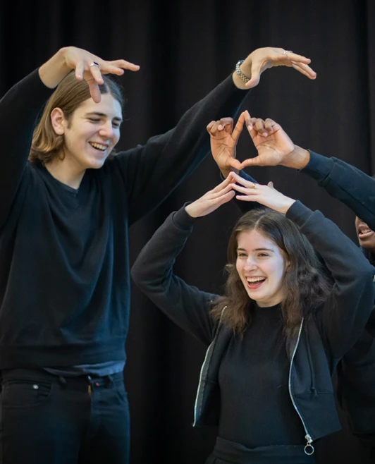 Three students building a creative pose with their hands and arms in a collaborative, playful performance moment during class. Three students building a creative pose with their hands and arms in a collaborative, playful performance moment during class.